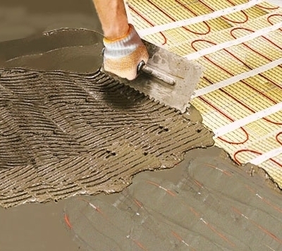 Po przykryciu maty 1,5 cm warstwą kleju do płytek, wyr&oacute;wnuje się go szpachelką murarską z ząbkami